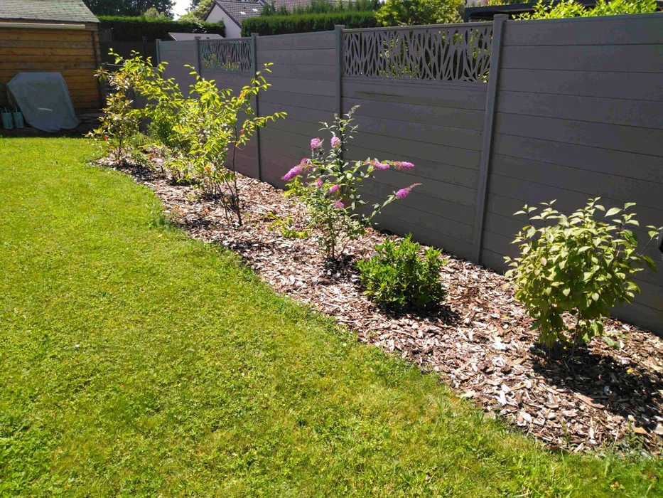 Jardin résidentiel ensoleillé avec bordure paysagère le long d'une clôture composite grise