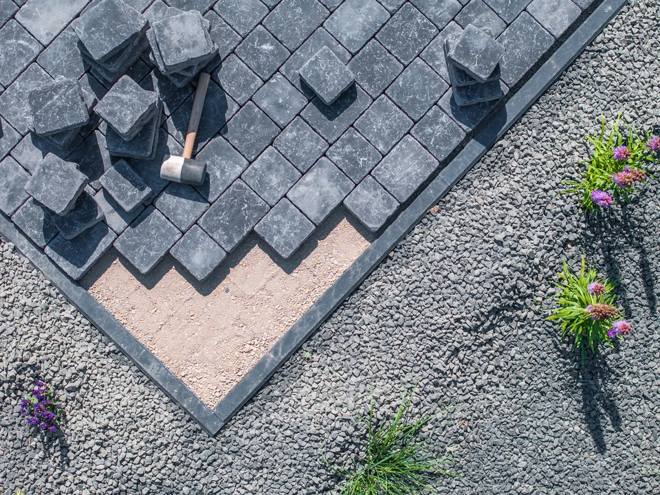 Chantier extérieur de pose de pavés en béton gris disposés en chevrons sur lit de sable stabilisé