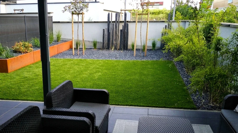 Jardin contemporain aménagé avec pelouse synthétique centrale, bordures en acier Corten rouillé, massifs en gravillon ardoise noire