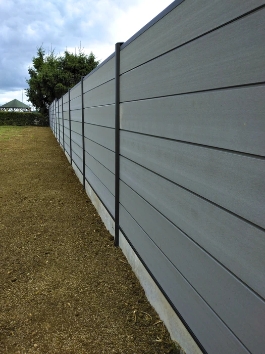 Une clôture moderne en panneau de couleur anthracite, une porte coulissante visible au garage et un guichet avec une boîte aux lettres