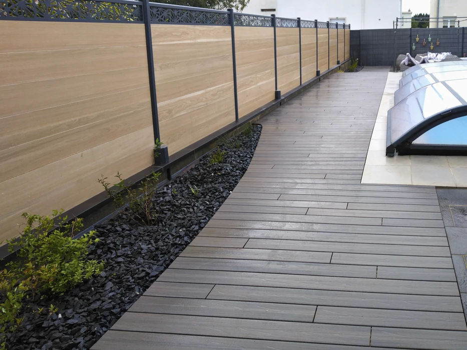 Scène extérieure montrant une clôture moderne avec panneaux en treillis bois naturel et poteaux métalliques anthracite