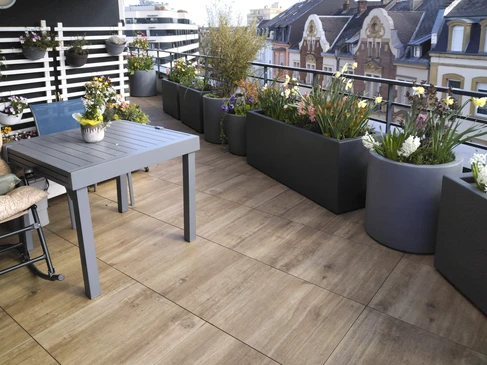 Terrasse extérieure aménagée avec salon de jardin en bois, jardin paysager en arrière-plan, bordures végétalisées et pots de fleurs colorées